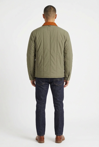 A man modeling a quilted utility jacket in olive green with a contrasting orange-brown corduroy collar, paired with dark blue jeans and brown leather shoes, against a plain white studio background.