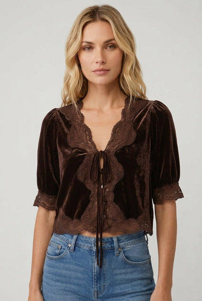 A woman wearing a dark brown velvet short-sleeve blouse with lace trim and a front tie detail, paired with blue jeans, against a plain white background.