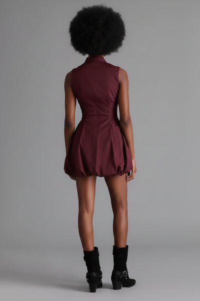 A model wears a sleeveless, button-up mini dress in a deep burgundy or maroon shade, styled with black ankle boots against a solid gray studio background.