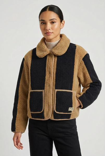 A cropped sherpa fleece jacket with a color-blocked design in tan and black, featuring a button-up front, a collar, and two front patch pockets, shown on a light gray background.